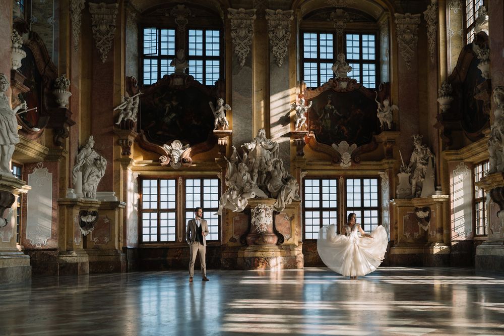 Ornate baroque ballroom with grand windows, chandeliers and decorative ceiling in a historic palace.