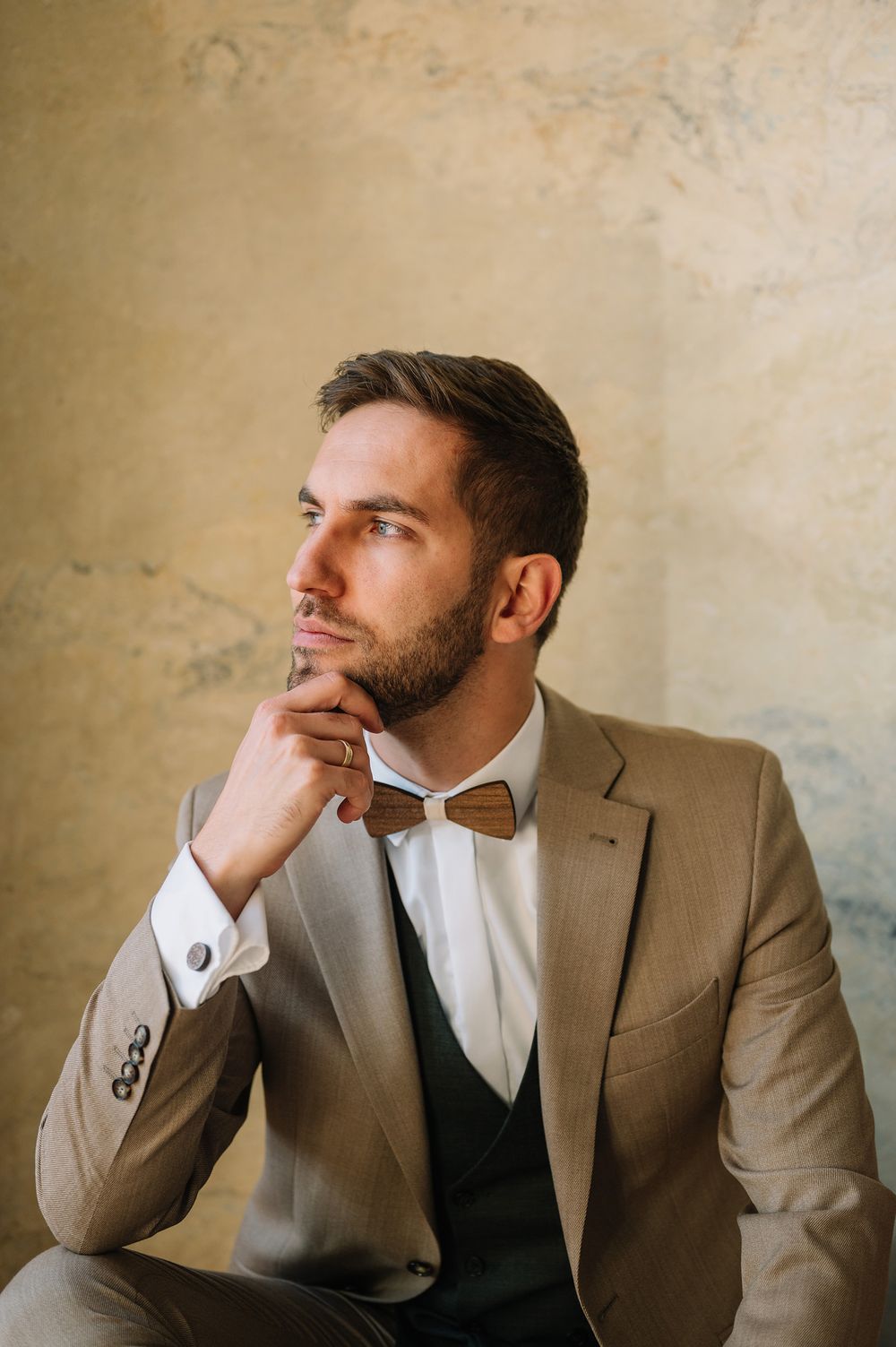 Thoughtful portrait in formal attire with bowtie against textured beige wall.