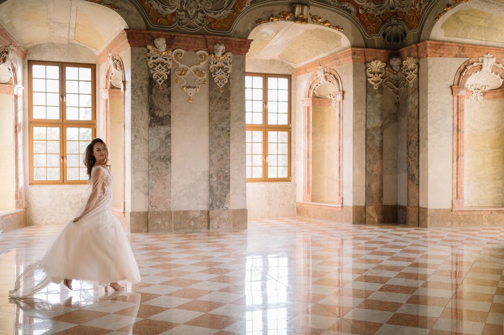 White dress flowing as figure spins in an ornate palace room with checkerboard floor and baroque details.