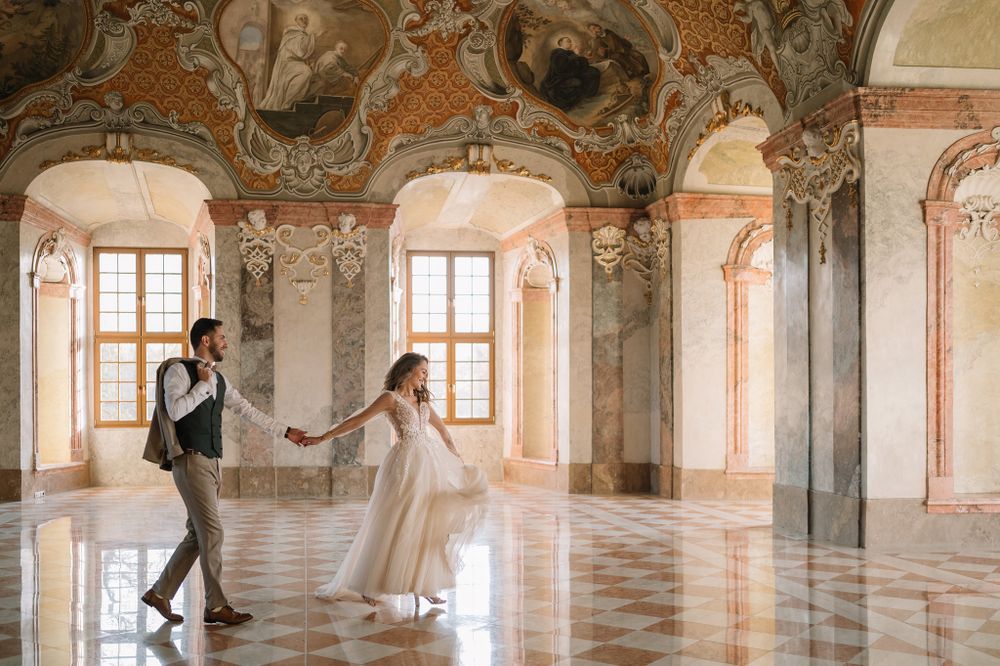Dancing couple in formal wear twirling across a grand baroque palace ballroom with ornate details.