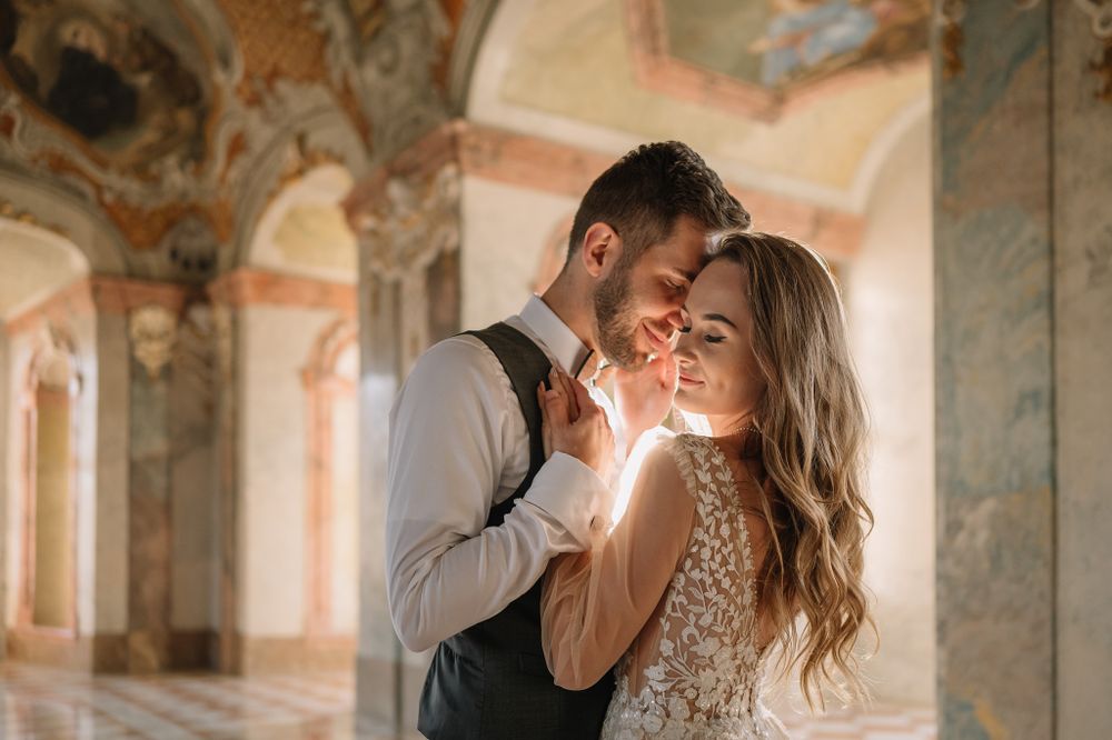Romantic couple in wedding attire sharing an intimate moment in an elegant palace hallway.