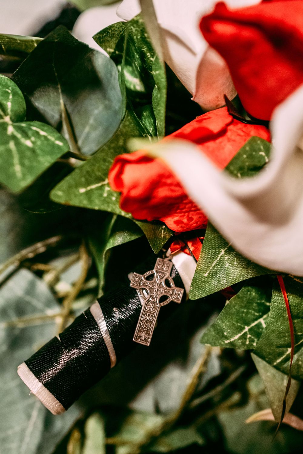 Celtic cross pendant and ring on green leaves with red rose petals.