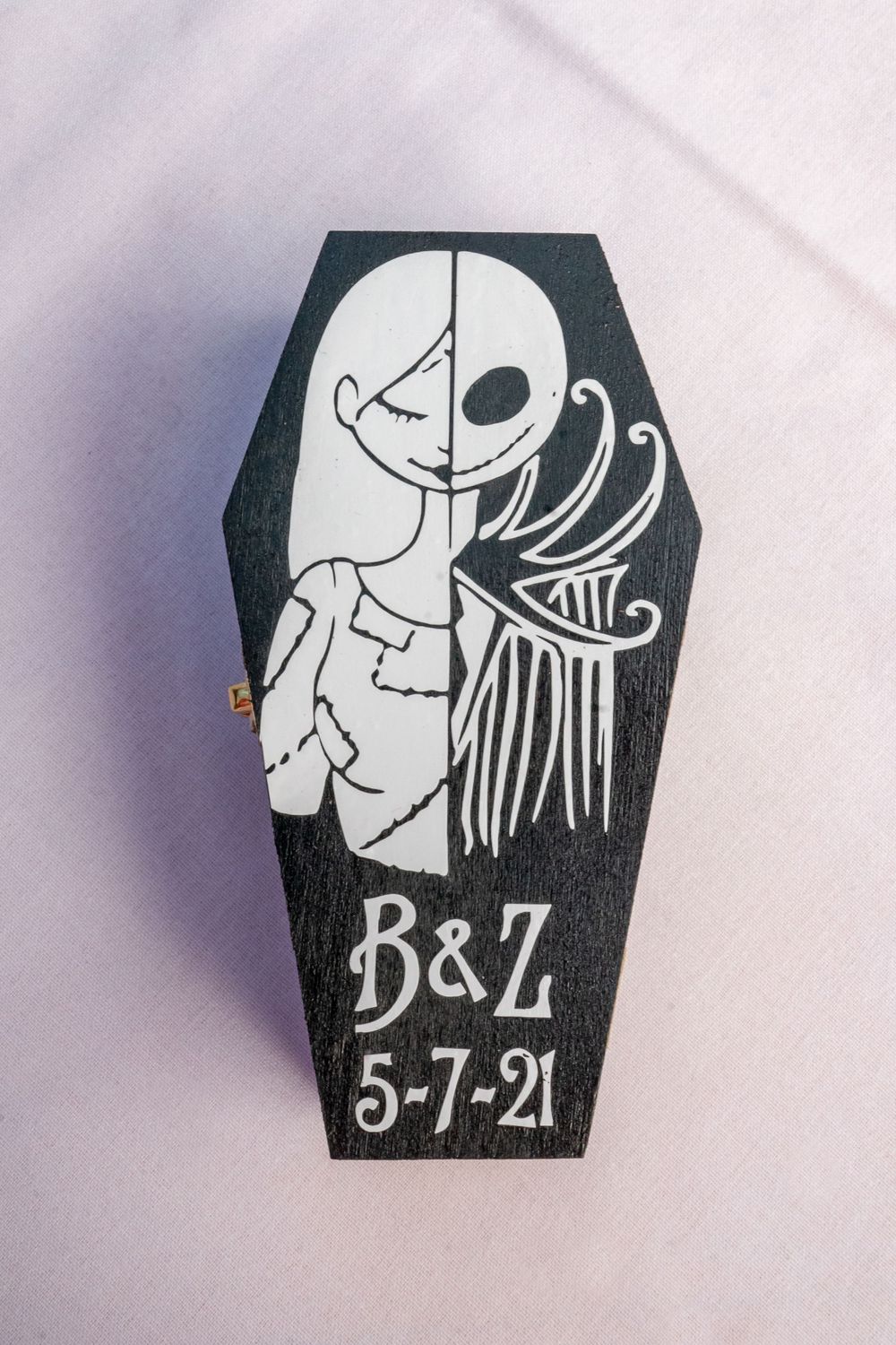 Black coffin-shaped decorative sign with white skeletal design and date 5-7-21.