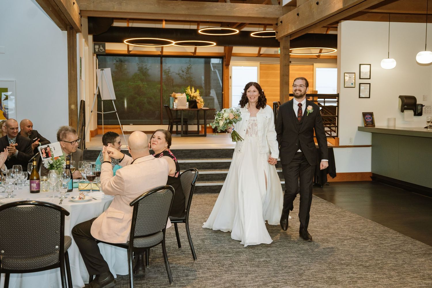 Melissa and Michael entering the reception room hand in hand, smiling, as seated guests applaud.