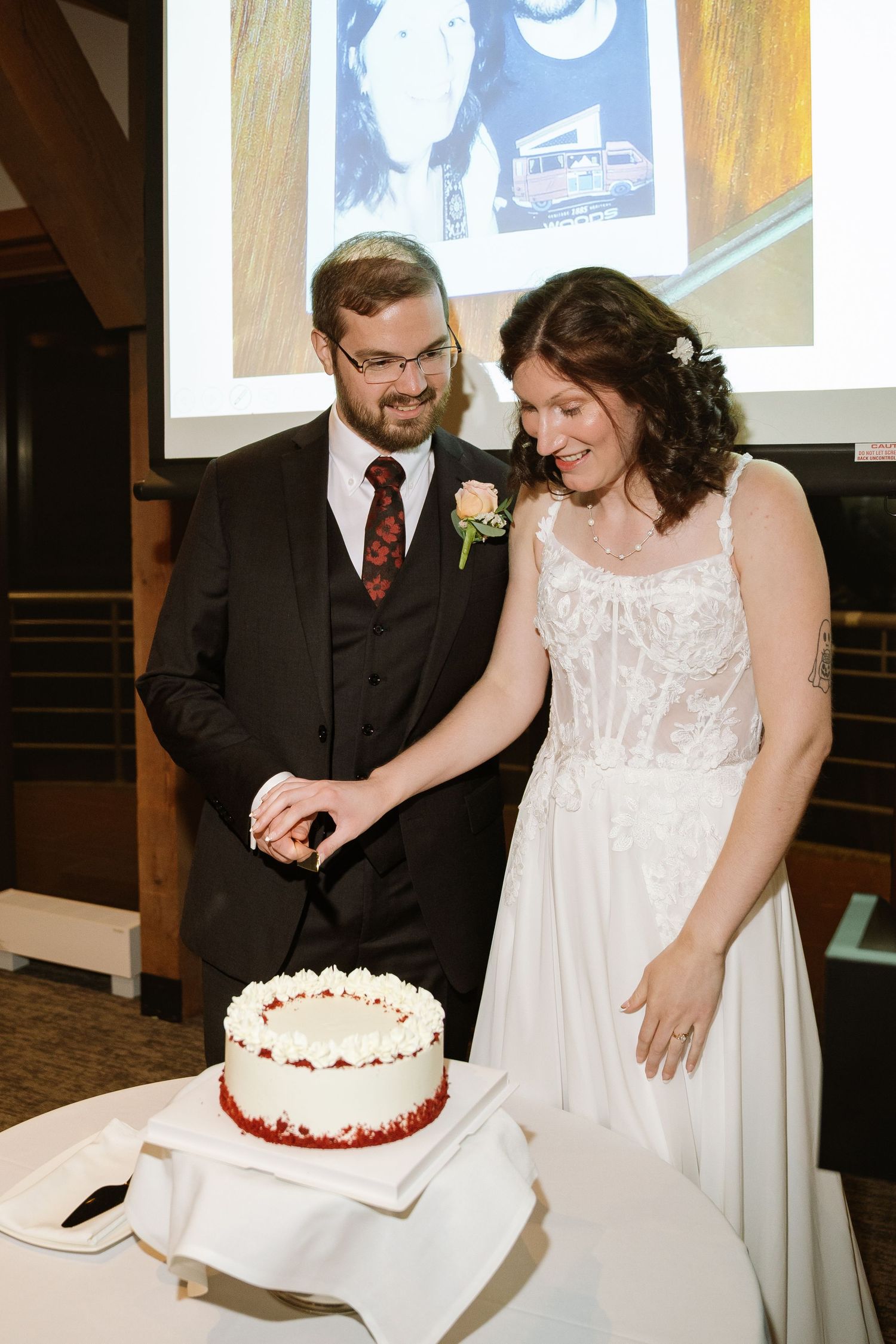 Michael and Melissa smiling as they cut their white wedding cake with red trim at the reception.