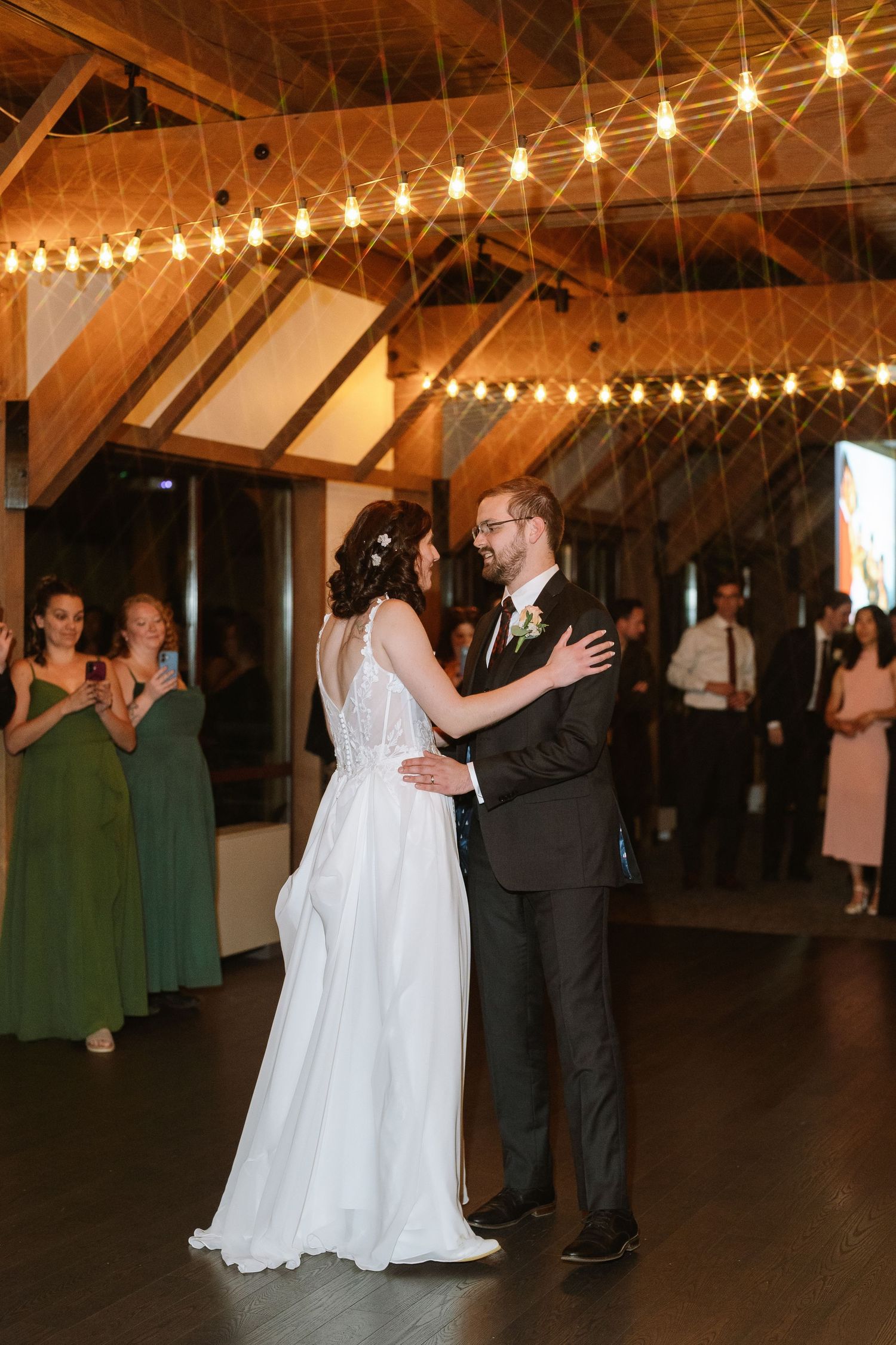 Michael and Melissa sharing their first dance under string lights at the reception, with guests watching.