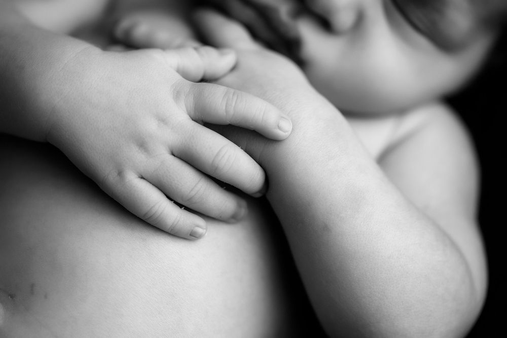 Black and white macro image of newborn baby boy's hands crossed across chest.