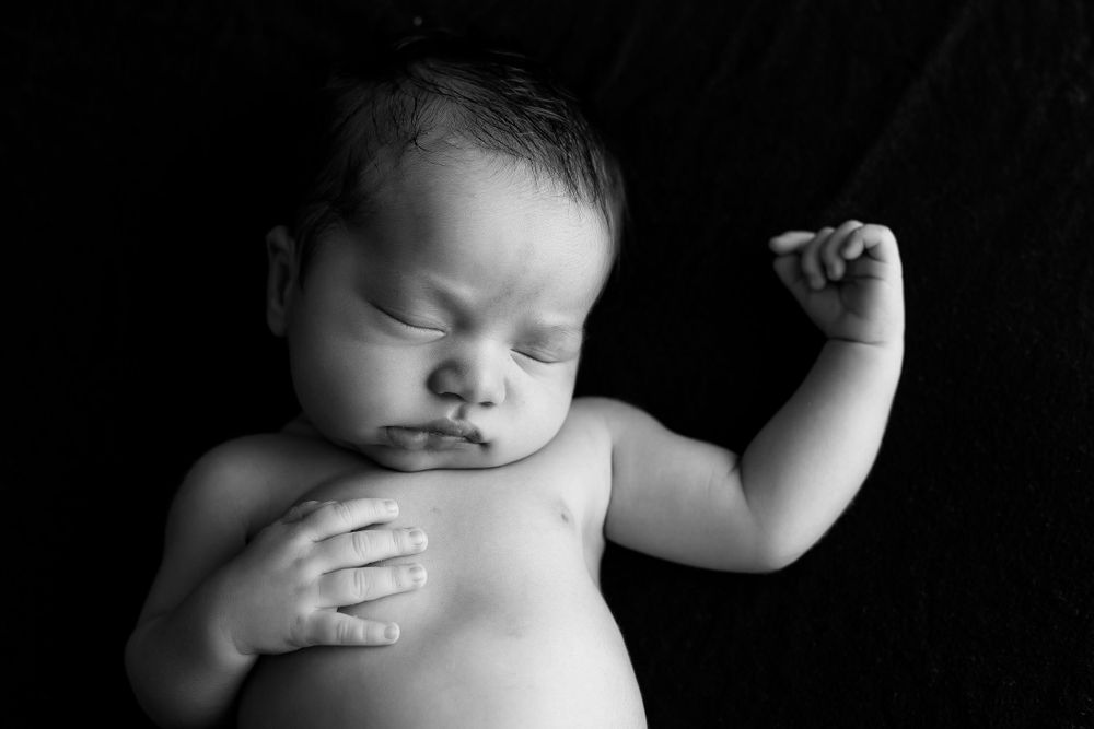 Black and white image of newborn baby born on black backdrop.