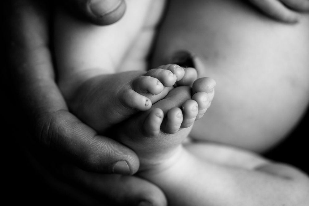 Black and white image of newborn baby boy's feet with dad's hand supporting them.