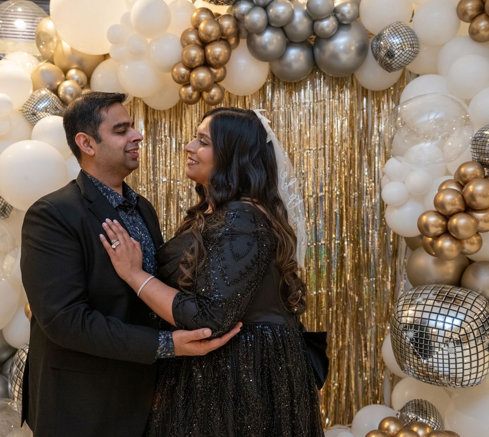 Couple sharing a romantic moment in front of a gold glitter and balloon party backdrop.
