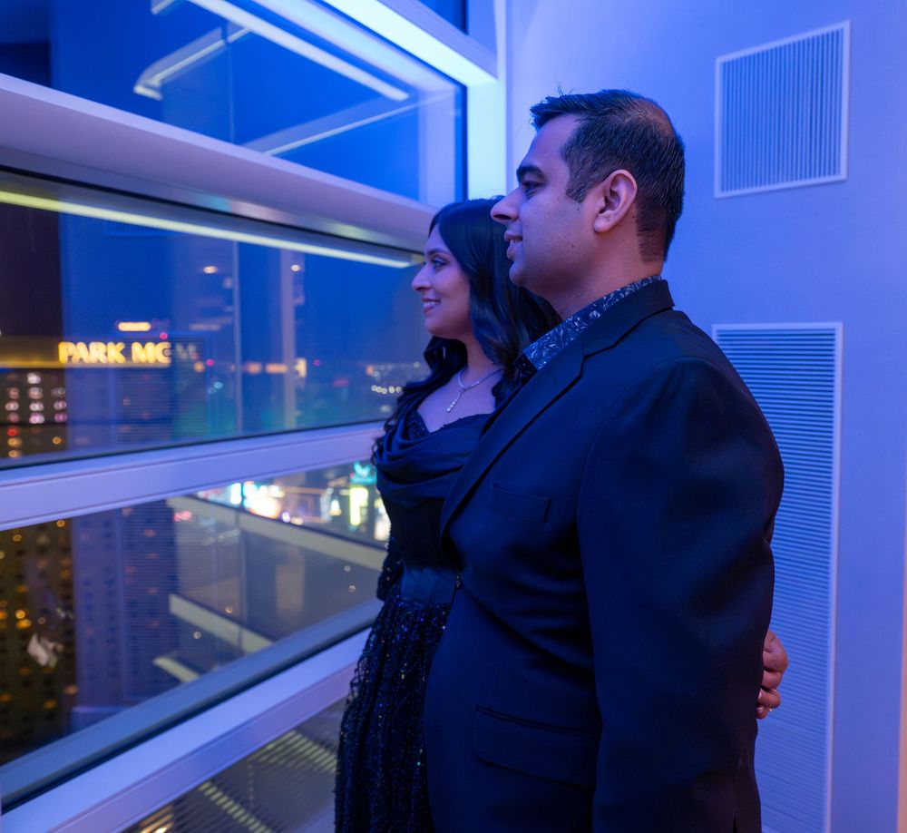 Couple standing together gazing at the Las Vegas city skyline through floor-to-ceiling blue-lit windows.