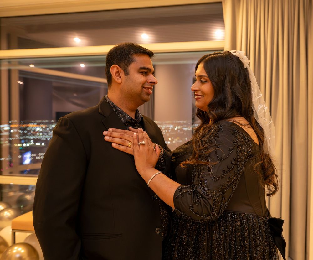Couple in matching black outfits sharing a romantic moment by a city view window at night.