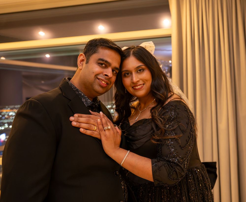 Smiling couple in black outfits posing together at an engagement party, woman showing off her ring.