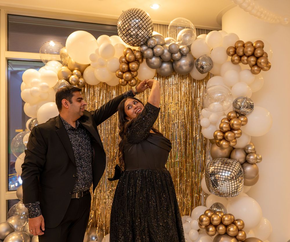 Couple posing with gold and silver balloon arch and disco balls at a glamorous New Year's Eve party.