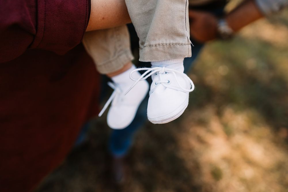 Baby in white lace-up shoes and khaki pants dangles in the air during a family photo session in Knoxville, TN.