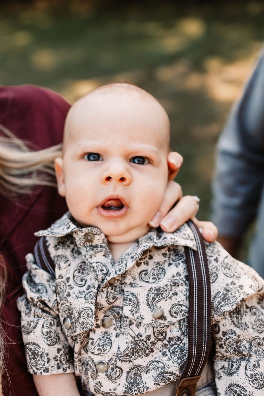 Wide-eyed baby in a paisley button-up shirt and brown suspenders during a family photo session in Knoxville, TN.