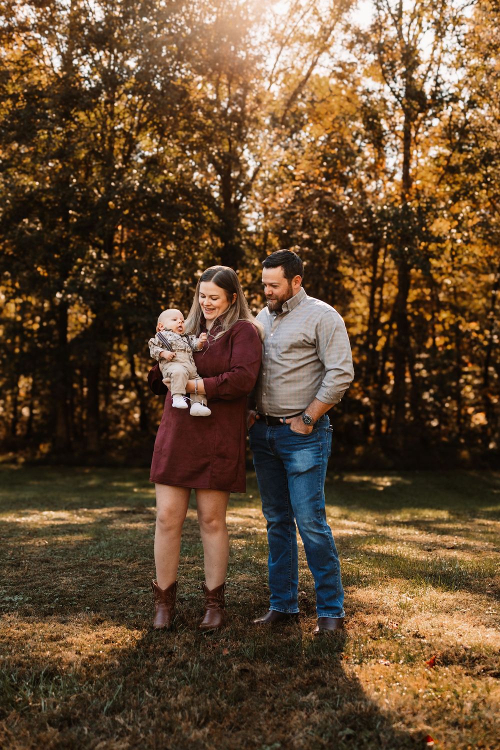 Young family of three poses outdoors in golden autumn light during a family photo session in Knoxville, TN.