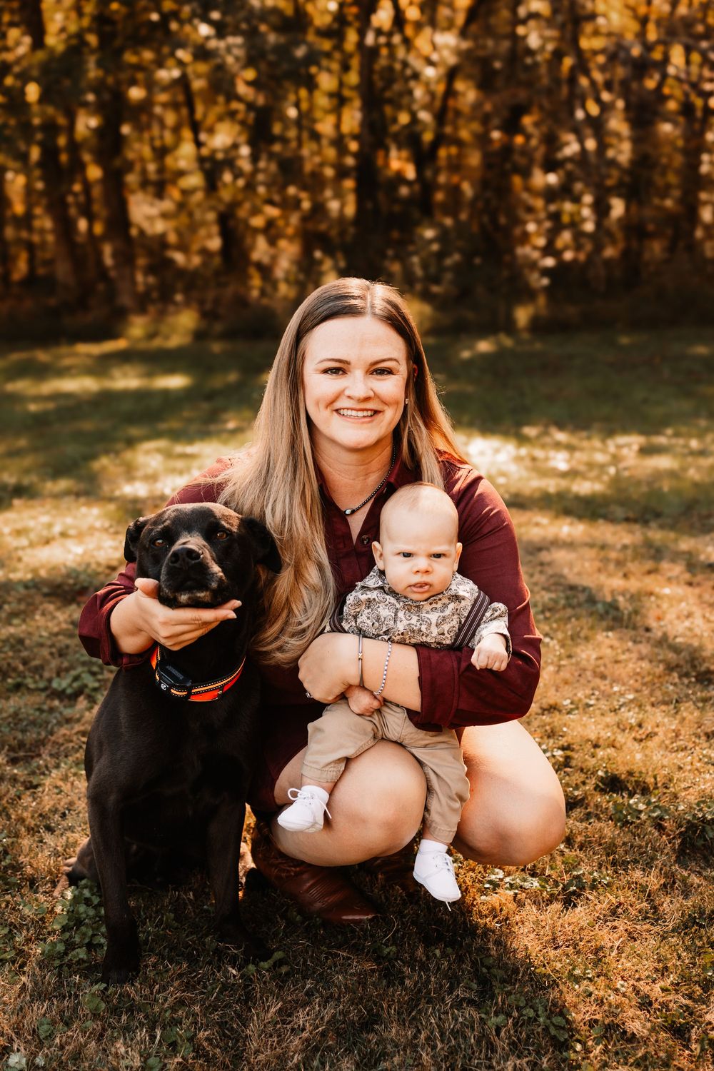 Smiling woman kneeling on grass in an autumn park, during a family photo session in Knoxville, TN.