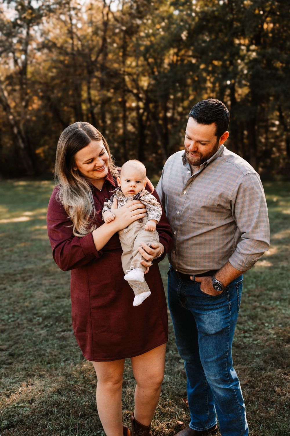 Smiling mother in a burgundy dress holds her baby beside the father iduring a family photo session in Knoxville, TN.