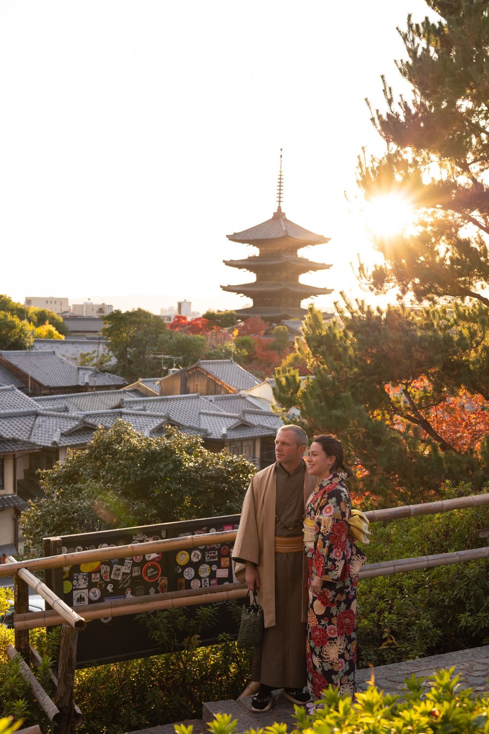 Couple in traditional kimono admire the Yasaka Pagoda at sunset among autumn foliage in Higashiyama, Kyoto, Japan.