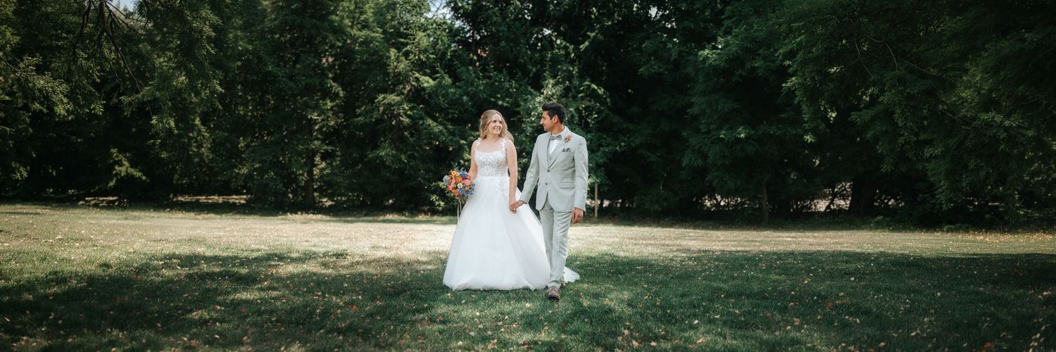 A couple in wedding attire stands together during golden hour in a scenic outdoor setting.