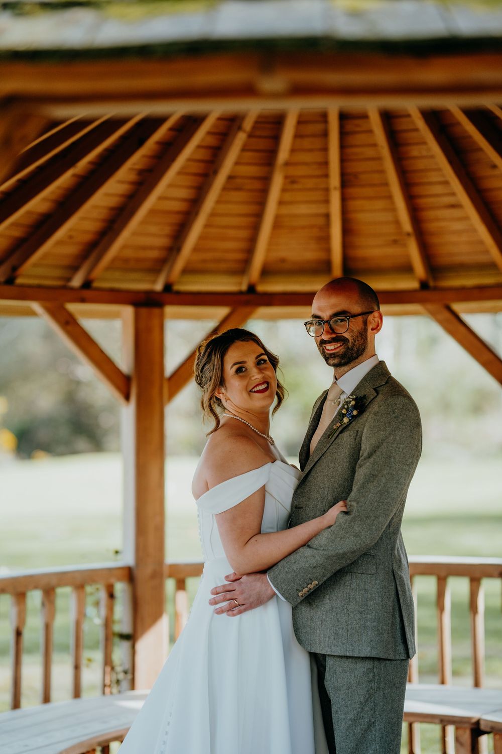 Smiling bride and groom embracing under a wooden gazebo on their wedding day.