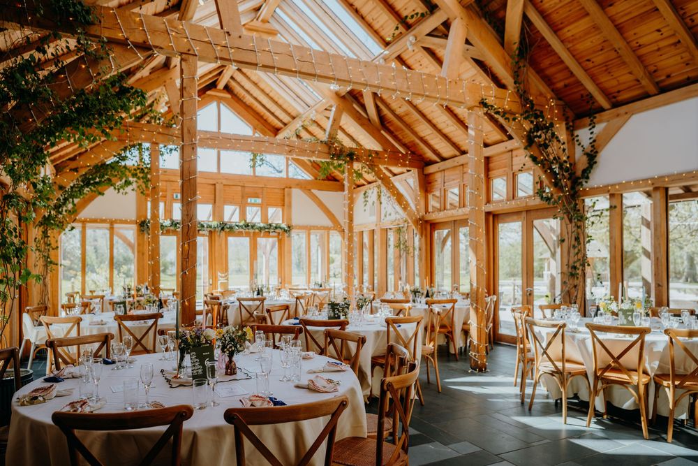 Elegant barn wedding reception venue with wooden beamed ceiling, round tables and floral decorations.