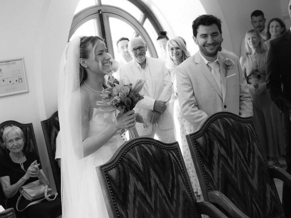 Black and white photo of a smiling bride and groom during their wedding ceremony, surrounded by guests.