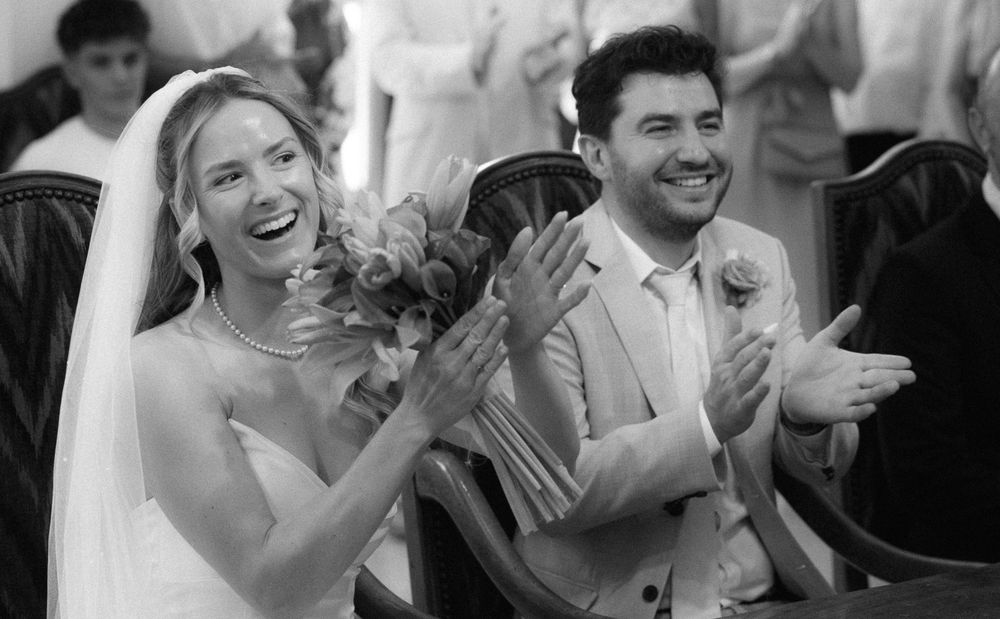 Black and white photo of a joyful bride and groom clapping and laughing during their wedding ceremony.