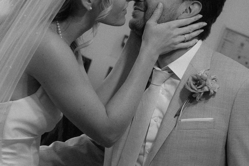 Black and white wedding photo of bride and groom sharing a romantic kiss, bride wearing veil and pearl necklace.