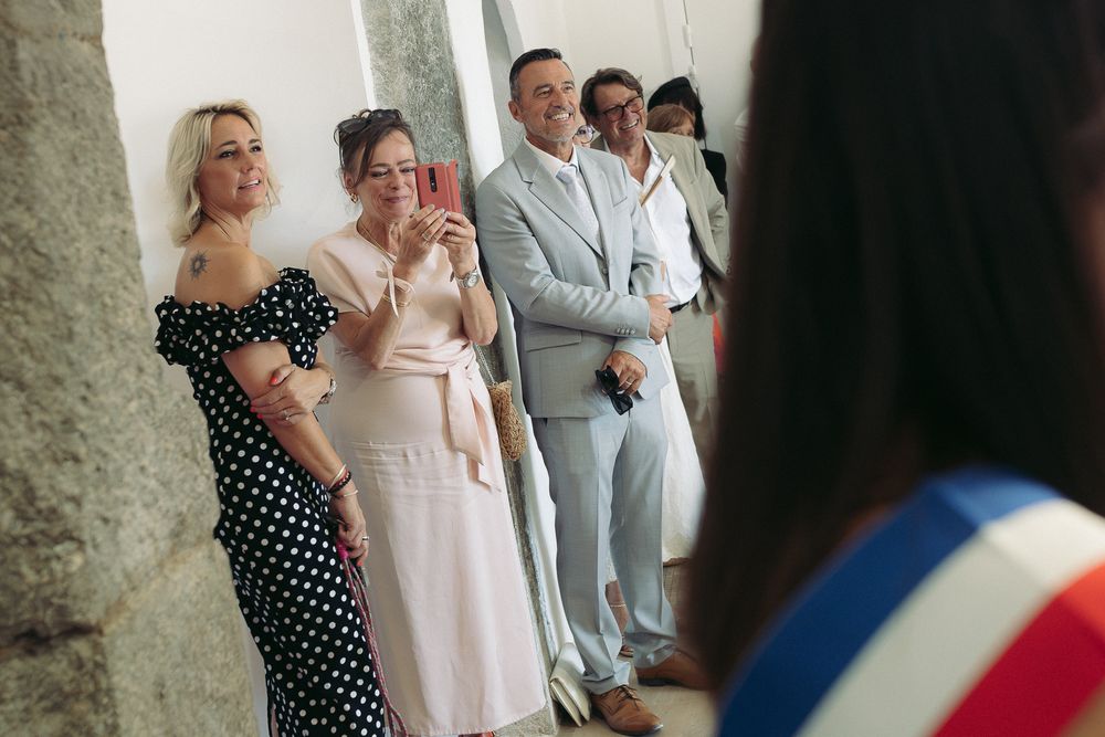 Guests smile and take photos at a French wedding ceremony, dressed in elegant attire including polka dot and pink dresses.