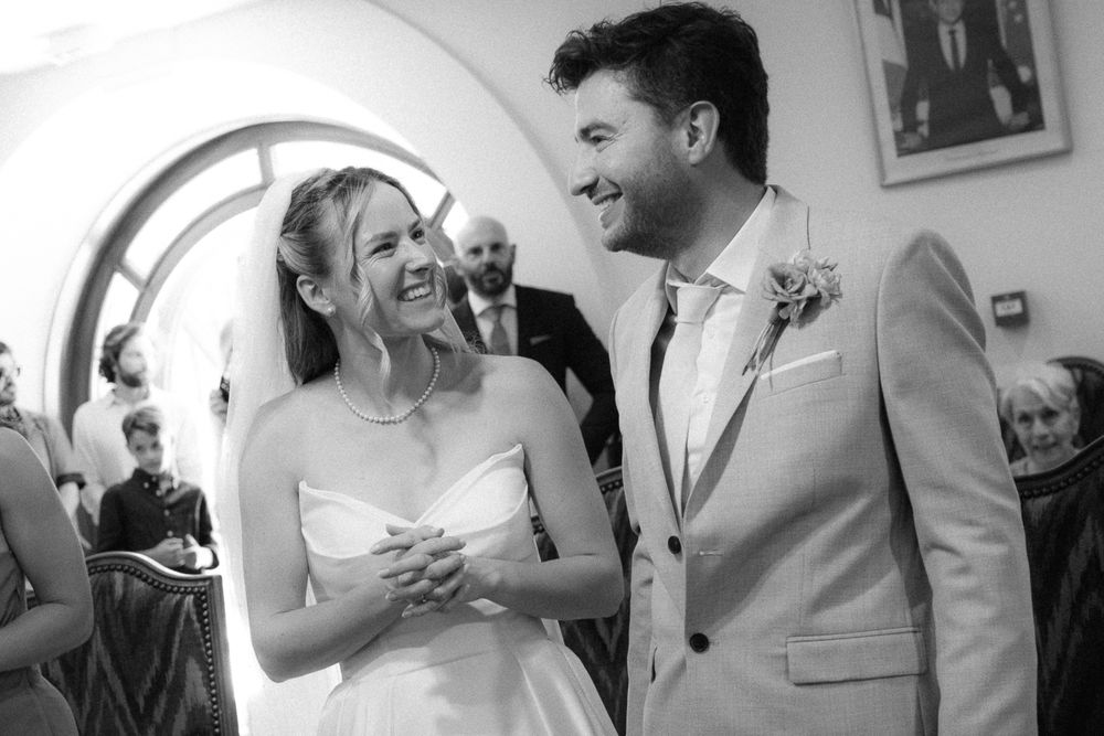 Bride and groom laughing joyfully during wedding ceremony in black and white photo.