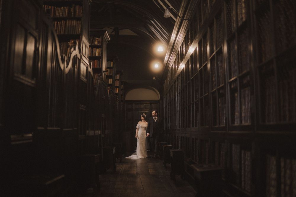 Bride and groom stand romantically in a dimly lit, wood-paneled library hall during their wedding.
