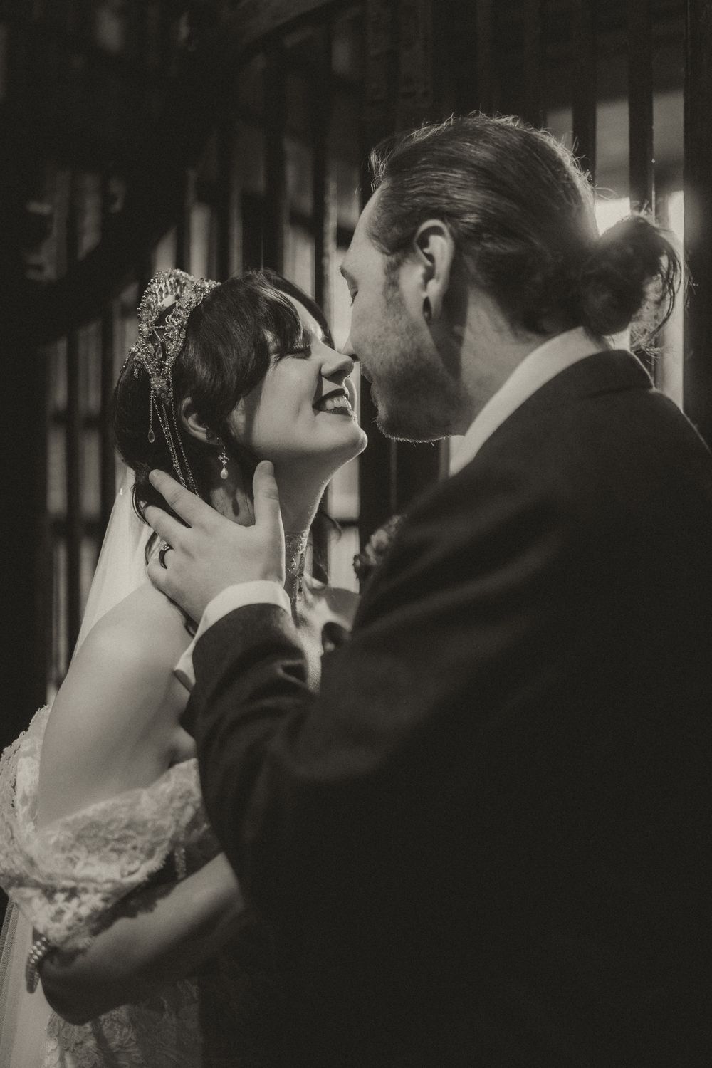 Black and white wedding photo of bride and groom sharing a romantic moment, groom tenderly holding brides face.