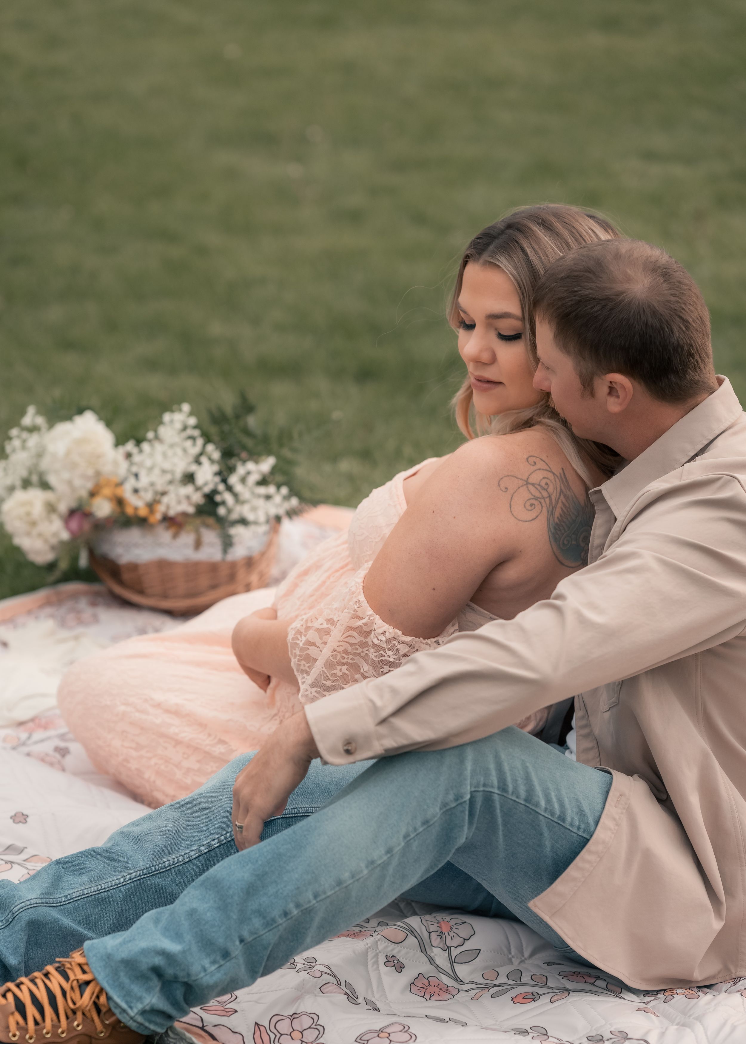 Couple sharing a romantic moment on a floral blanket during an outdoor picnic with wildflowers in soft natural light.