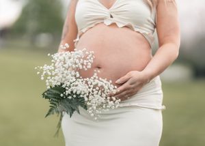 Pregnant woman in white crop top holding baby's breath bouquet outdoors for maternity photo shoot.