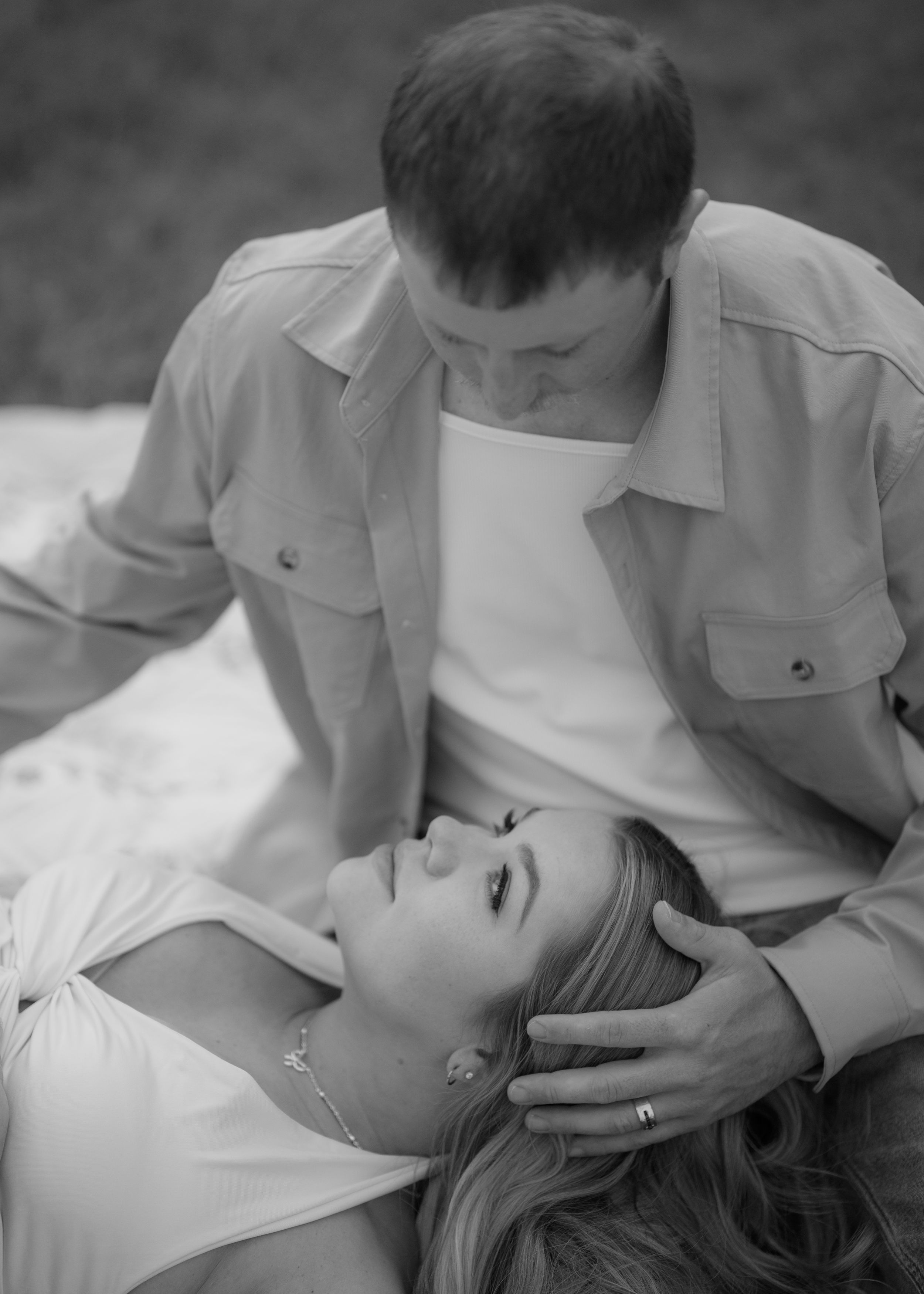 Black and white maternity photo of couple sharing intimate moment, woman lying down as partner gently holds her face.
