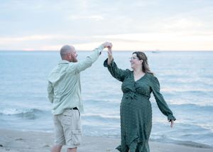 Couple dancing on beach at sunset, man spinning woman in green dress near ocean shoreline.