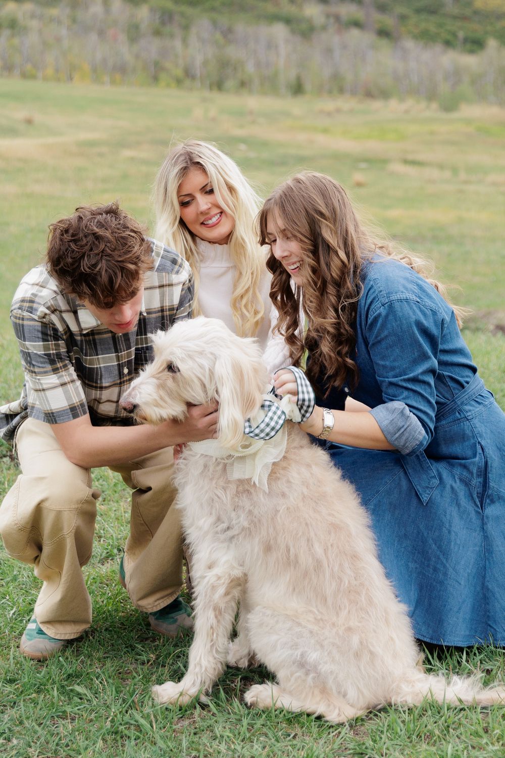 A family with two teens and a fluffy white dog enjoy a playful outdoor moment on a grassy field.