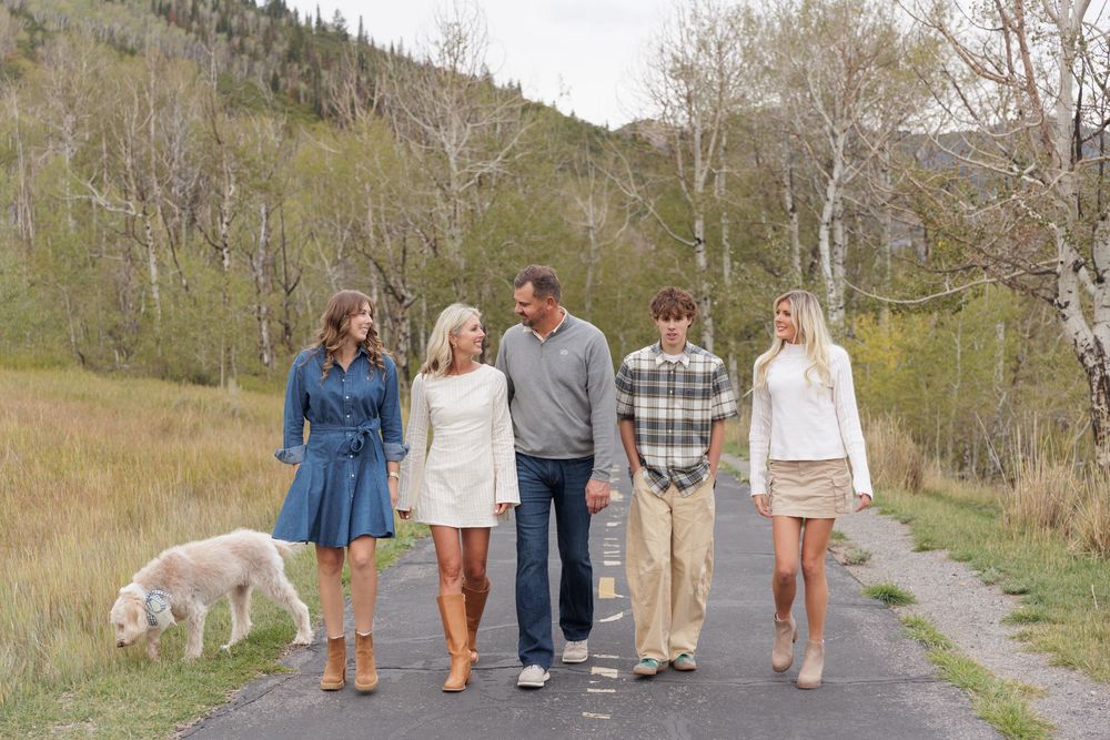 A happy family of five strolls along a scenic path with their white fluffy dog in autumn.