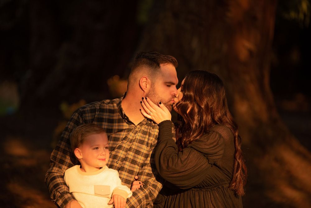 Couple sharing a tender moment with their young child outdoors in warm evening sunlight.