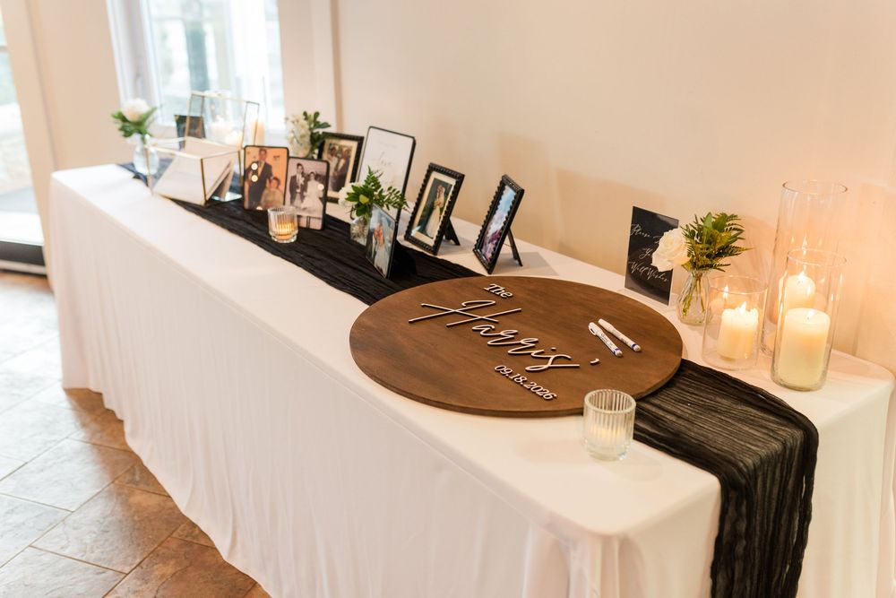 Elegant wedding memory table with framed photos, candles, and a round wooden sign on a white linen-covered table.