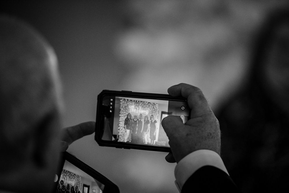 Black and white photo of hands holding a smartphone capturing a group photo at an event.
