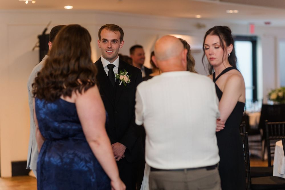 Wedding guests in formal attire gather and converse in an elegant white reception venue.