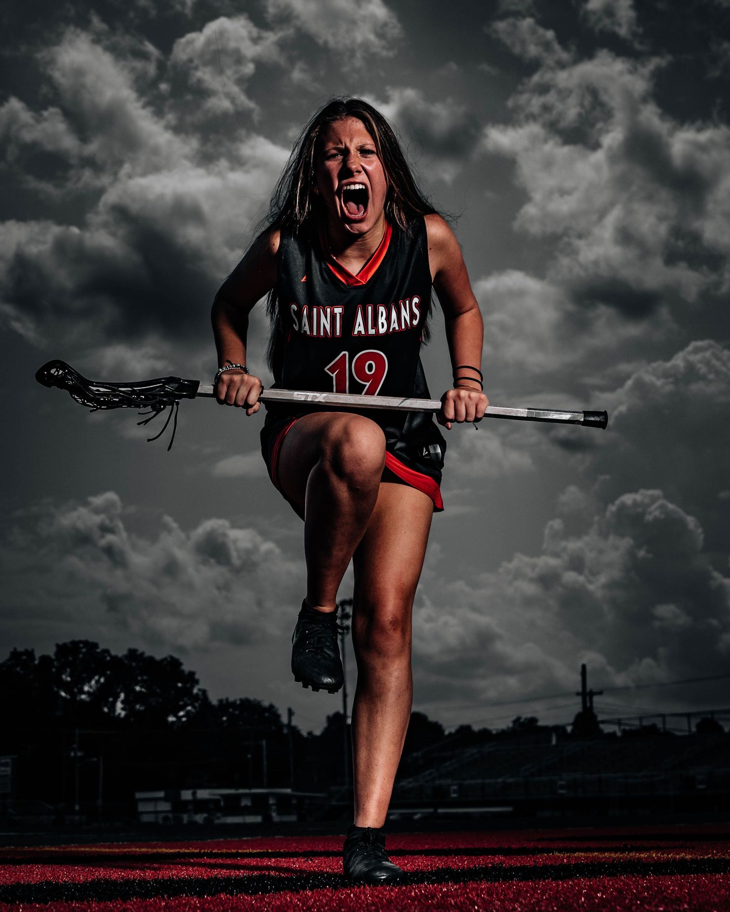 Saint Albans #19 female lacrosse player poses aggressively with stick under dramatic stormy sky.