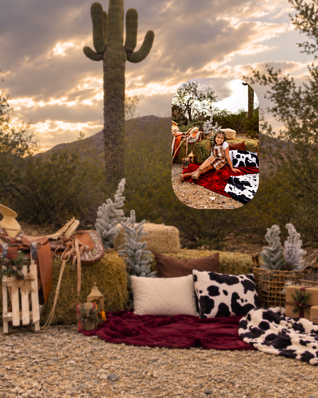Western Christmas photo setup in the Arizona desert with a saguaro cactus, cowhide pillows, saddle, hay bales, and a child on a red blanket.