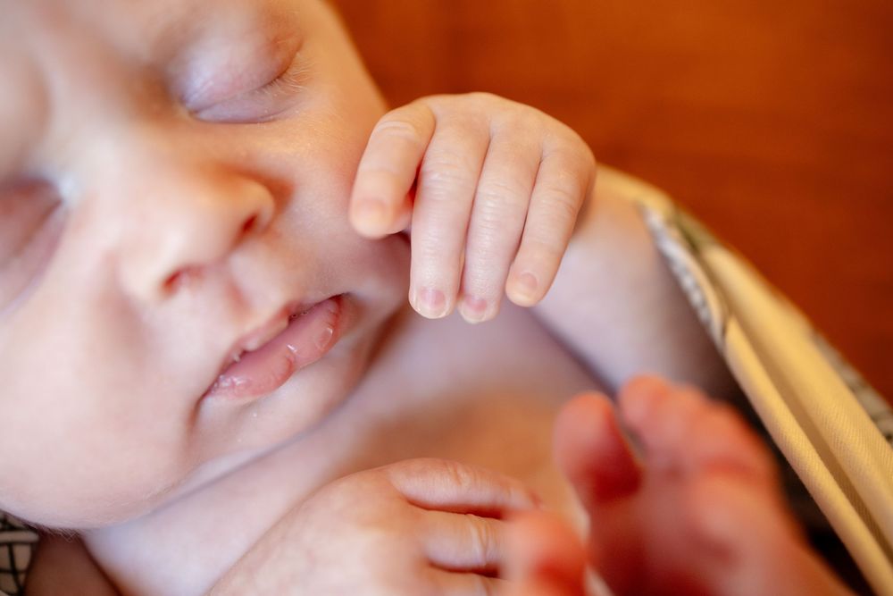 Close-up of a sleeping newborn baby with eyes closed, lips slightly parted, and tiny hand resting near the face.