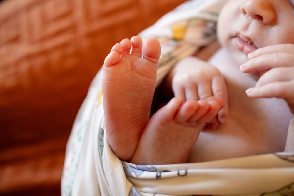 Close-up of a newborn baby's tiny feet and hands wrapped in a soft patterned blanket against a warm orange background.