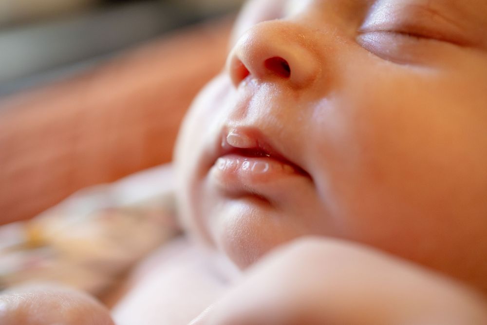 Close-up of a sleeping newborn baby's face with closed eyes, a tiny nose and soft lips resting peacefully.