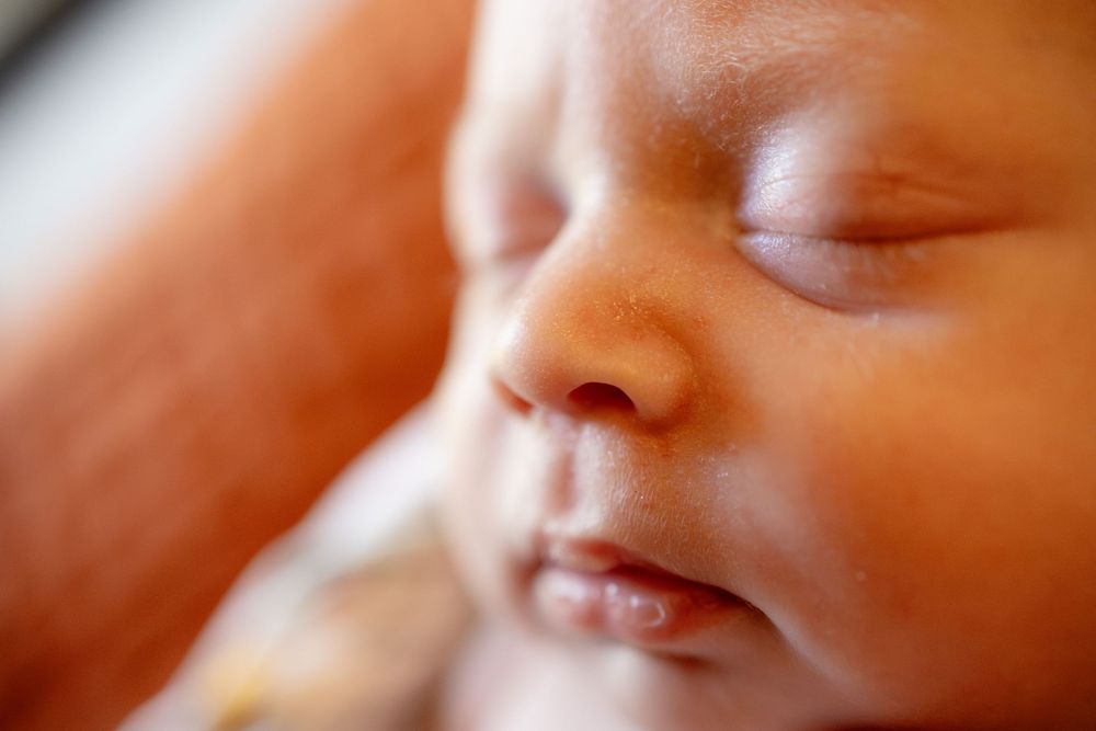Close-up of a sleeping newborn baby with closed eyes and soft, peaceful facial expression resting in a parent's arms.